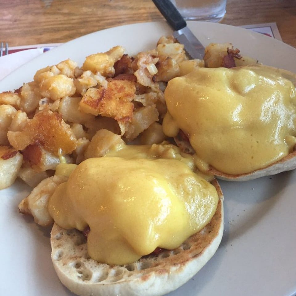 Eggs Benedict with hollandaise sauce and a side of home fries on a white plate at New Britain Diner.