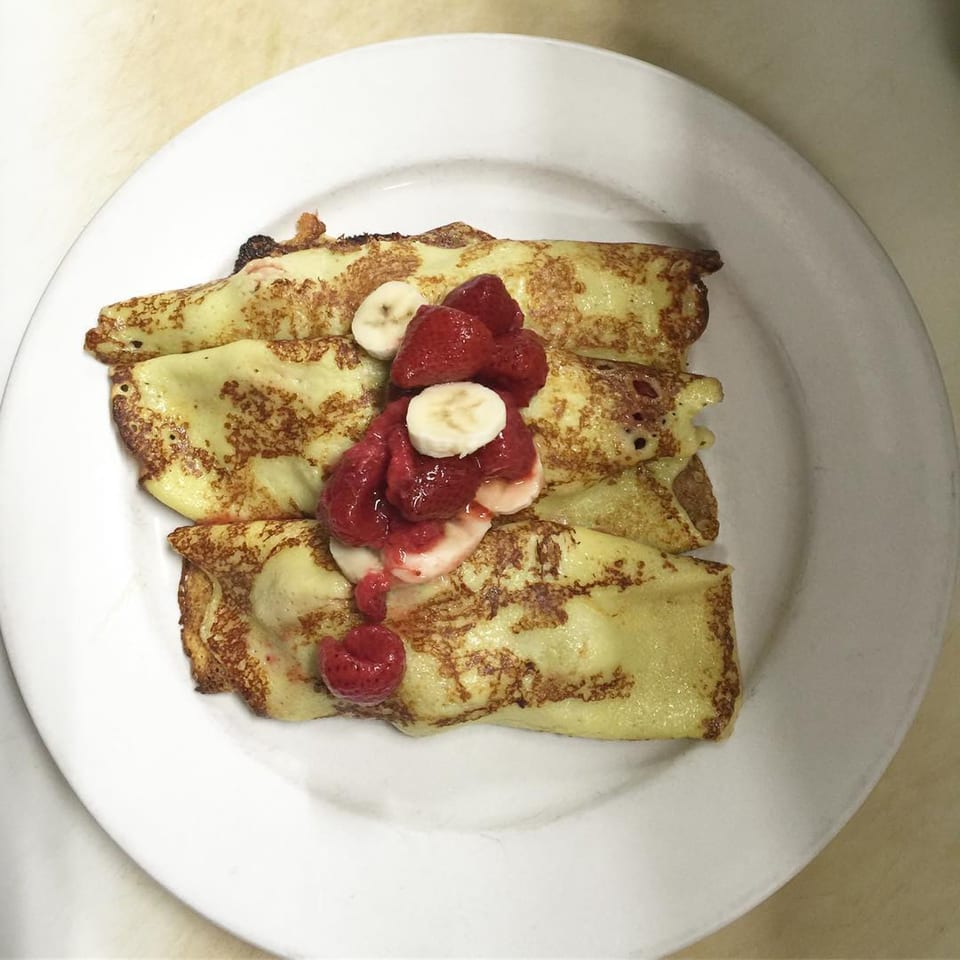 Three golden-brown crepes topped with fresh strawberries and banana slices on a white plate.