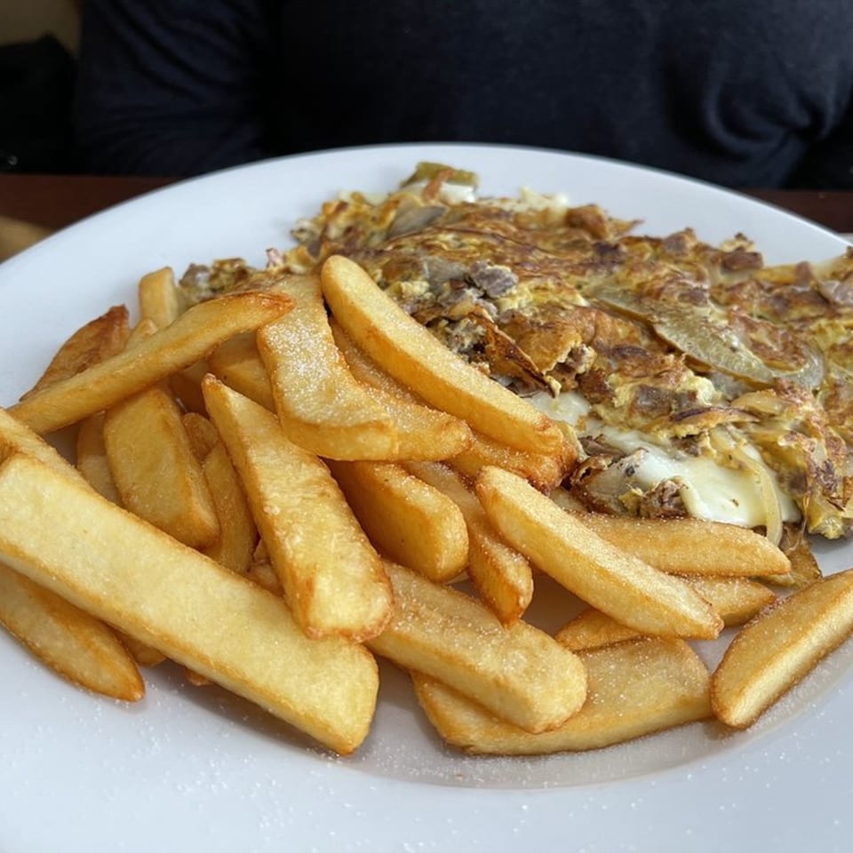 A diner plate with golden french fries and a cheesy omelet with onions and meat.
